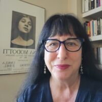 patrice petro headshot Patrice Petro, the Dick Wolf Director of the Carsey-Wolf Center appears against a background of a bookshelf and a poster featuring Tina Modotti. She is wearing a black v-neck blouse, glasses, and dangly earrings.